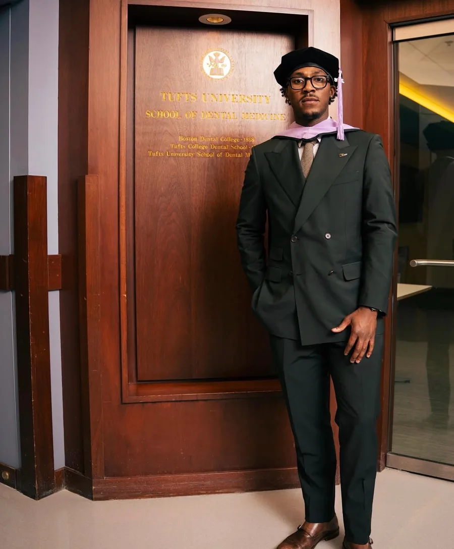 A client in a dark green double breasted suit and doctoral regalia, by a wooden door.
